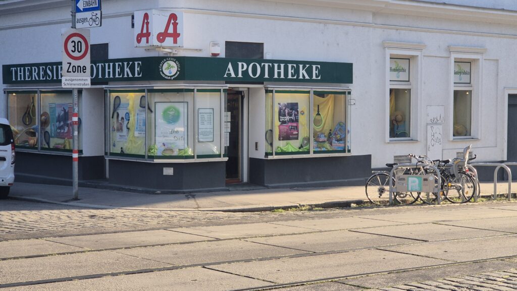 Eckhaus mit Apotheke und grüner Fassadenbeschriftung an einer sonnigen Straßenkreuzung
