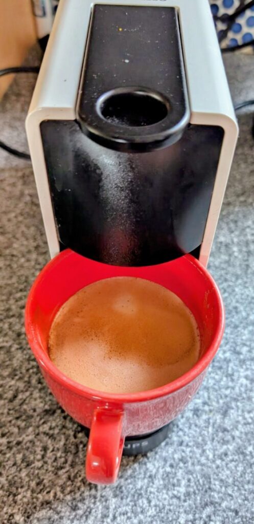 Große rote Tasse mit frisch gebrühtem Kaffee unter einer Kaffeemaschine
