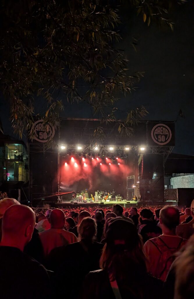 Rot beleuchtete Open-Air-Bühne bei Nacht mit Publikum davor